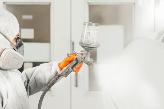 Male worker sprays paint with spray gun on car body part in car maintenance service paint room. photo