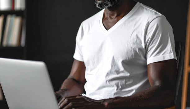 Middle-aged man wearing white V-neck T-shirt working on laptop photo