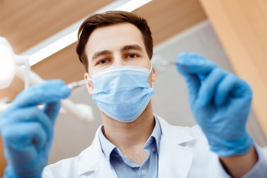 Dental treatment, teeth care and medicine. Young attractive dentist in white coat, protective mask and rubber gloves treats teeth to patient, in modern interior clinic, bottom view, close up photo
