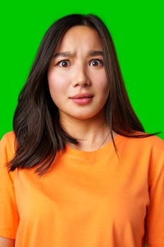 Young woman with surprised expression wears orange shirt on bright green background photo