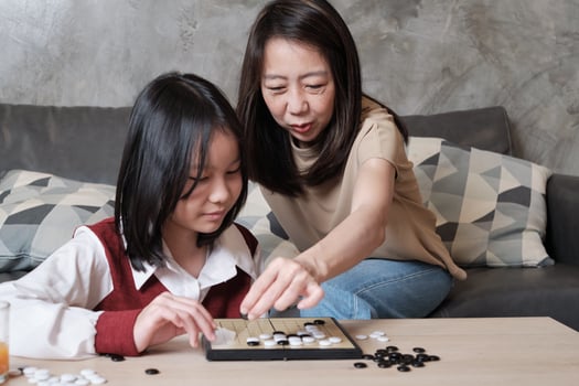 Asian family, single mum, fun playing Go with child, checkers board game on table in home living room together with love and cheerful, happy weekend relaxing hobby of kid and parent. photo