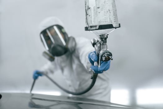In protective mask and wear. Close ,up, view of man that is painting a car by using spray guy photo