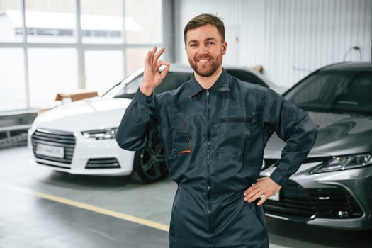 Handsome, friendly ,guy. Repairman in uniform is standing in the garage with cars photo