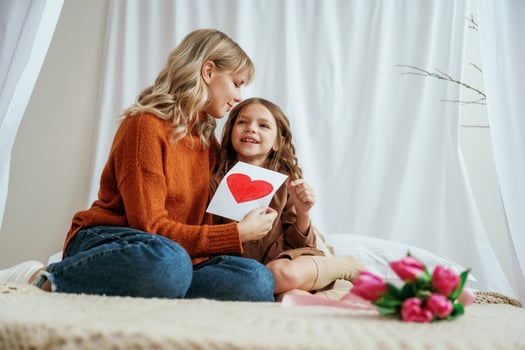 Red paper, heart ,,shaped present for mother's day. Female parent with daughter is at home photo