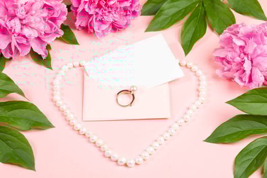 Wedding invitation envelope surrounded by peonies and pearls, romantic flatlay, bridal promotions. photo