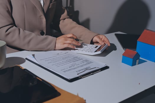 A woman is sitting at a desk with a laptop and a house model photo