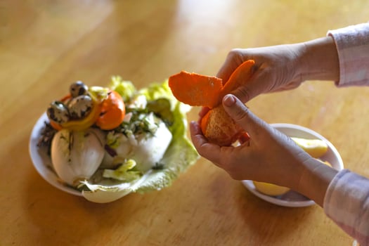 female hands peeling tangerine over food waste container photo