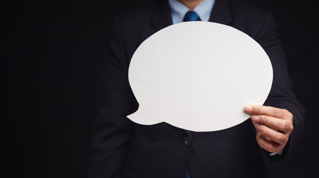 Close-up of a businessman in a suit holding a blank white speech bubble while standing on a black background. Space for text. photo