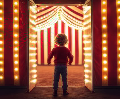 Child stands before a brightly lit circus entrance at night photo