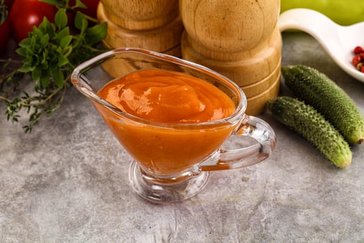 A glass of tomato sauce next to a pepper and cucumber photo