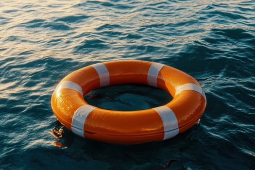 Bright orange lifebuoy floating on calm blue water at sunset photo