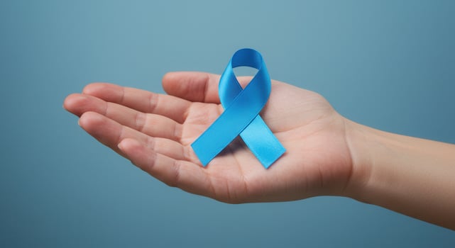 Hand holding a blue ribbon on blue background. Symbol of prostate cancer awareness, mens health awareness, world diabetes day, and bullying prevention. photo