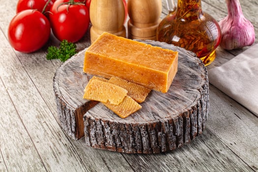 A piece of cheese on a wooden block with tomatoes and garlic photo