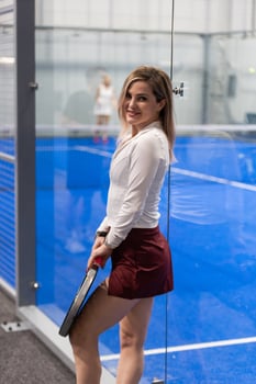 Woman playing padel in a blue grass padel court indoor - Young sporty woman padel player hitting ball with a racket photo
