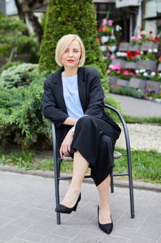 Woman dressed in business style sits on a chair and looks at the camera. The woman has a break in the middle of the working day photo
