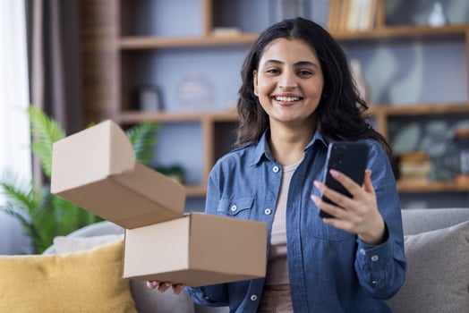A young woman is sitting at home, excited to receive her recent order and holding her smartphone for sharing online. photo