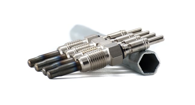 A set of four glow plugs next to a wrench, all against a clean, white background. photo