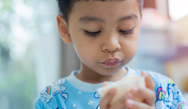 Young Asian boy sit in living room and eating while playing at daytime. Selective focus. photo
