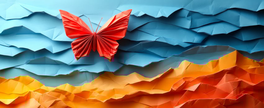 Colorful butterfly on a landscape. A vibrant red butterfly crafted from paper hovers above a textured, multicolored landscape of blue and orange hues. photo