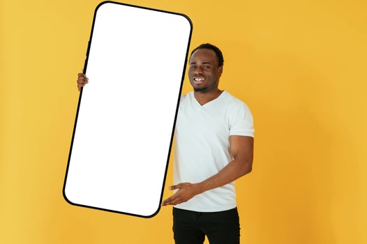 With very,, big smartphone, for copy space. Black man is in the studio against yellow background photo