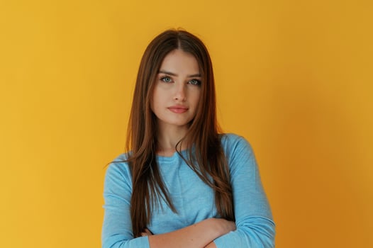 Arms crossed, standing. Young woman is against yellow background photo