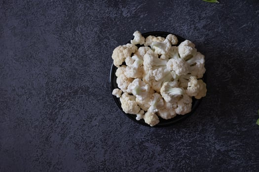 Raw cauliflower, black pepper peas and a wooden spoon with coarse salt lie on a gray background. Selective focus. Vegetable layout. Copy space. The view from the top. photo