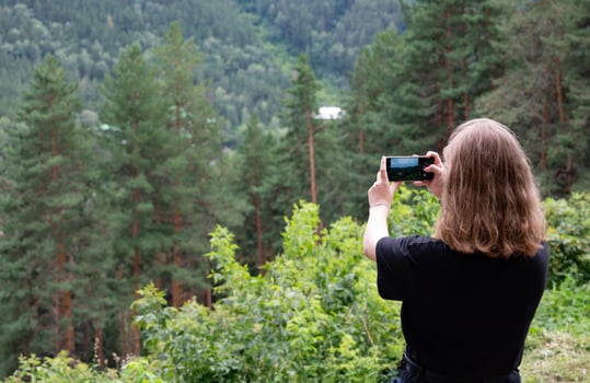 Pretty traveling woman standing on top of mountain at sunset and using mobile phone. High mountains touristic path. Digital communication. photo