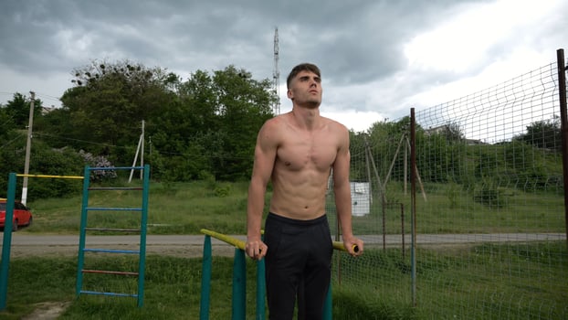 Young sportsman doing push ups on parallel bars at nature.Strong sporty man exercising at sports ground. Male shirtless athlete training hard outdoor. Concept of active sportive lifestyle. Slow mo photo