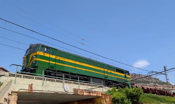 Green train crossing an overpass in a sunny landscape near a mountainous area during daytime photo