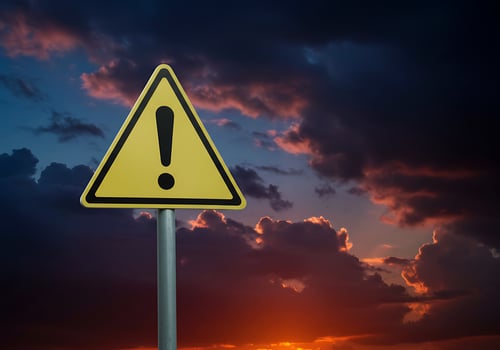 A yellow warning sign with an exclamation mark against a dark sky photo