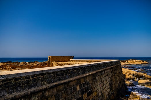 A stone wall borders a rocky coastline under a blue sky, where the ocean stretches out to meet the distant horizon photo