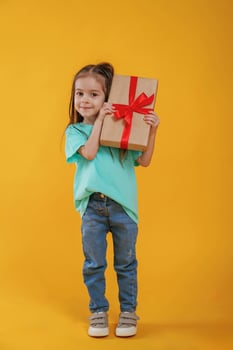 Present in,hands,, gift box. Cute little girl is against yellow background photo