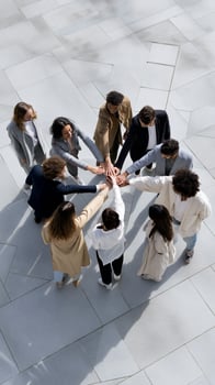 Diverse group joining hands in a circle on light-colored pavement. Teamwork, unity, collaboration, and support are evident photo