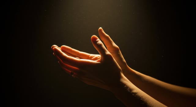 Warm light illuminates womans hands in prayer or gratitude against a dark, textured background, conveying peacefulness and spirituality. photo