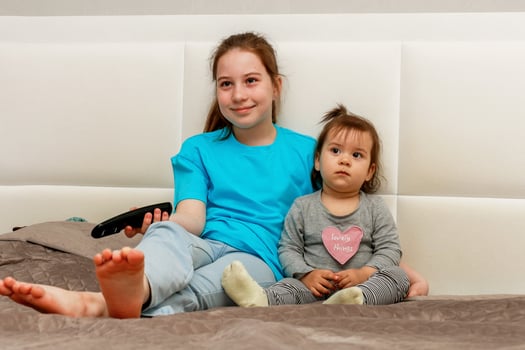 two sisters, younger and older, sitting on the bed watching TV photo