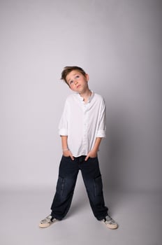 Monochrome image of a young boy standing barefoot on a plain backdrop, arms crossed, with a confident and slightly defiant look. Stark lighting adds depth and contrast. photo