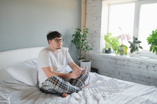 man in home clothes sitting on bed playing games holding controller photo