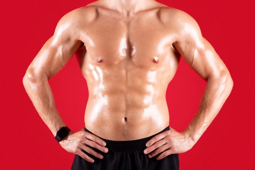 Cropped view of handsome young sportsman with bare torso posing with hands on hips over red studio background. Sexy athletic guy with prominent abs muscles, closeup view. Strength workout concept photo