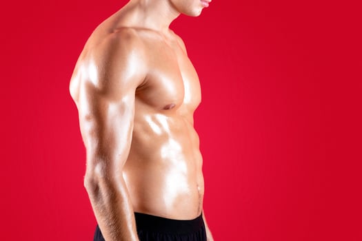 Unrecognizable young sportsman with bare torso and strong abs muscles posing on red studio background. Cropped view of shirtless millennial guy with sexy body. Strength training concept photo
