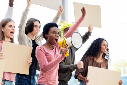 Multiethnic young demonstrators striking on the street, holding megaphone and empty placards. International group of people with blank banners protesting outdoors, defending human rights, side view photo