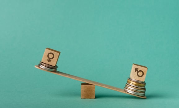 Gender pay gap. Wooden cubes with male and female gender signs on seesaw with different stacks of coins, men outweigh, copy space photo
