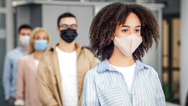 New normal and temperature check before work. Millennial multiracial employees in protective masks stand in line with social distancing at office in morning, free space, blurred, indoors photo