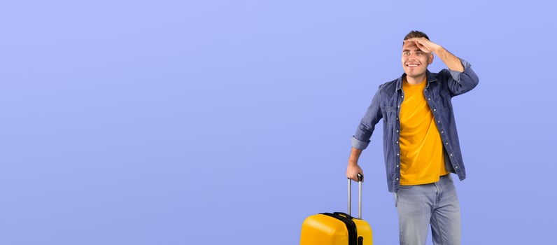Full length portrait of happy male traveler with luggage looking at empty space over blue studio background. Positive young tourist with suitcase ready to board his airplane flight photo