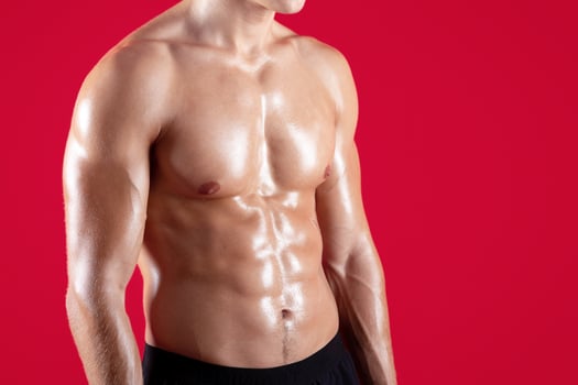 Closeup view of young strong sportsman with naked torso and prominent abs muscles on red studio background. Fit millennial guy with sexy body, cropped view. Strength workout concept photo