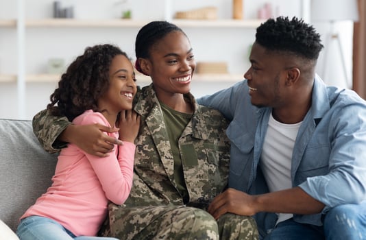 Loving attractive black woman in camouflage uniform mother having conversation with her family happy teen daughter and cheerful husband, sitting on couch all together and talking, home interior photo