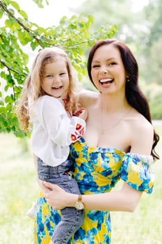 Young beautiful mother hugs her cute daughter, holds her in her arms, standing in the park near a tree photo