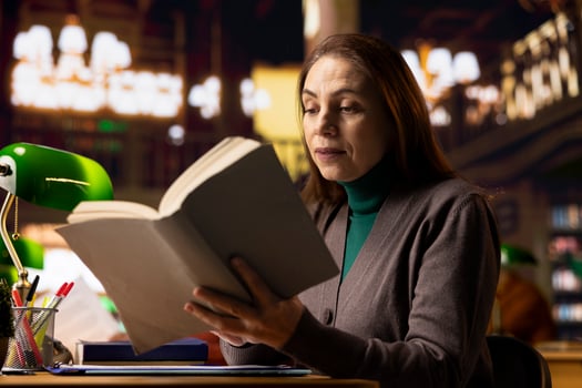 Mature female student in a work room surrounded by books and documents, preparing for a master dissertation and researching academic materials at the campus library. Higher education. photo