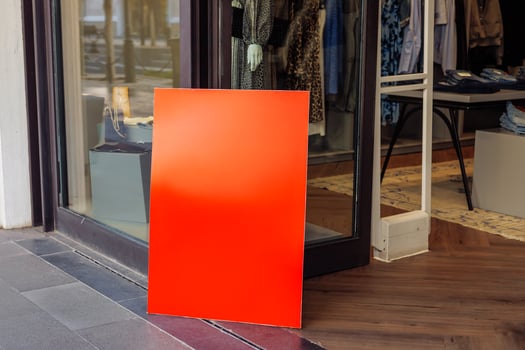red sign stands outside a storefront during midday in an urban shopping area photo