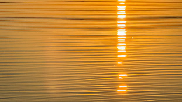 Golden sunset reflection on rippling water creating a warm tranquil ambiance with striking horizontal light patterns on the surface photo