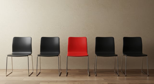 Row of five modern chairs against a beige wall, four black and one red. Concept for standing out, leadership, unique perspective and job interview. photo